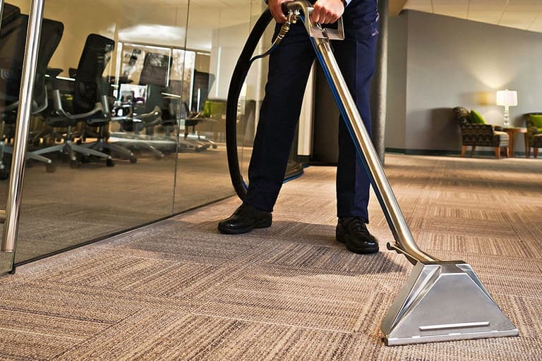 Professional cleaning technician deep cleaning patterned office carpet with an extraction wand.